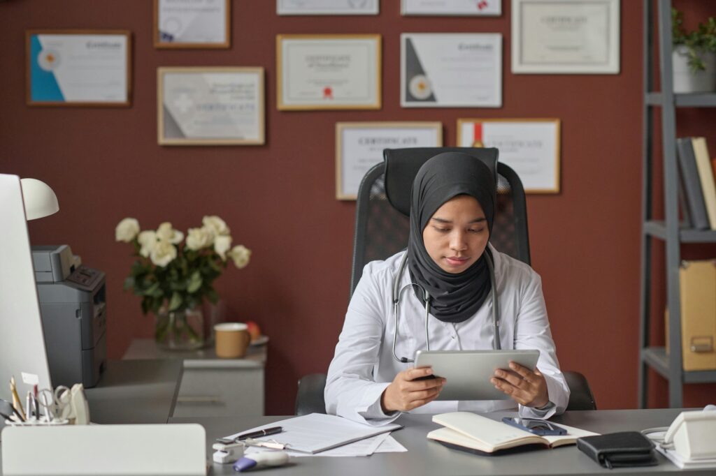 Female Physician in Hijab Working with Tablet at Her Desk in Clinic